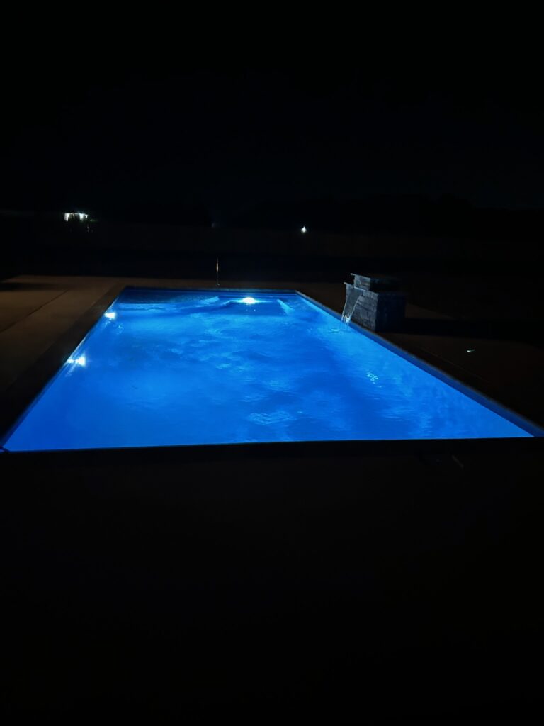 A lit swimming pool at night with surrounding darkness and slight reflections on the water's surface.