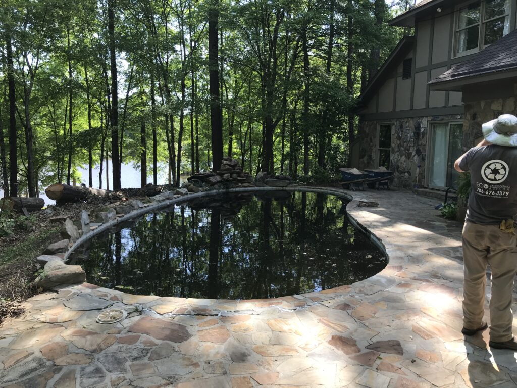 A person stands beside a small, oval pool surrounded by stone tiles