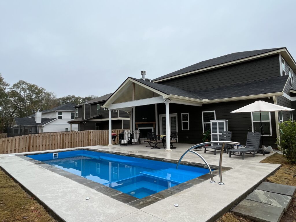 Backyard view of a modern house featuring elegant touches by a skilled swimming pool contractor, complete with a small pool, cozy lounge chairs, and a stylish patio area under a covered section.