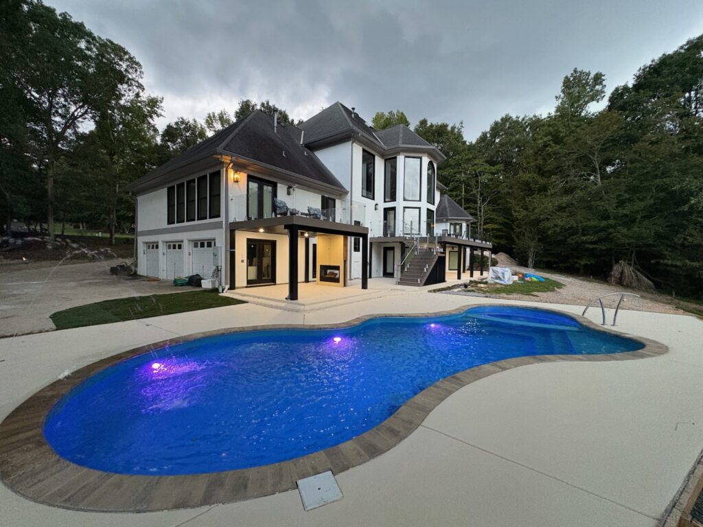 Modern two-story house with large windows and an attached garage, featuring a lit backyard pool with purple lights, surrounded by trees.