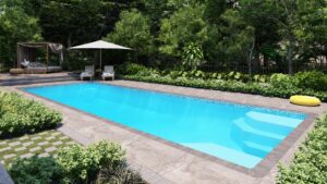Rectangular outdoor swimming pool with clear blue water, surrounded by plants, lounge chairs under an umbrella, a cabana, and a yellow inflatable ring.