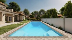 Rectangular outdoor swimming pool with clear water, surrounded by a paved deck, lawn, a beige house on the left, trees, and a white privacy fence on the right.