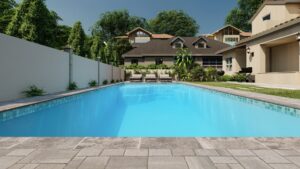 Rectangular outdoor swimming pool with clear blue water, surrounded by a stone patio, lounge chairs, greenery, and residential houses in the background.