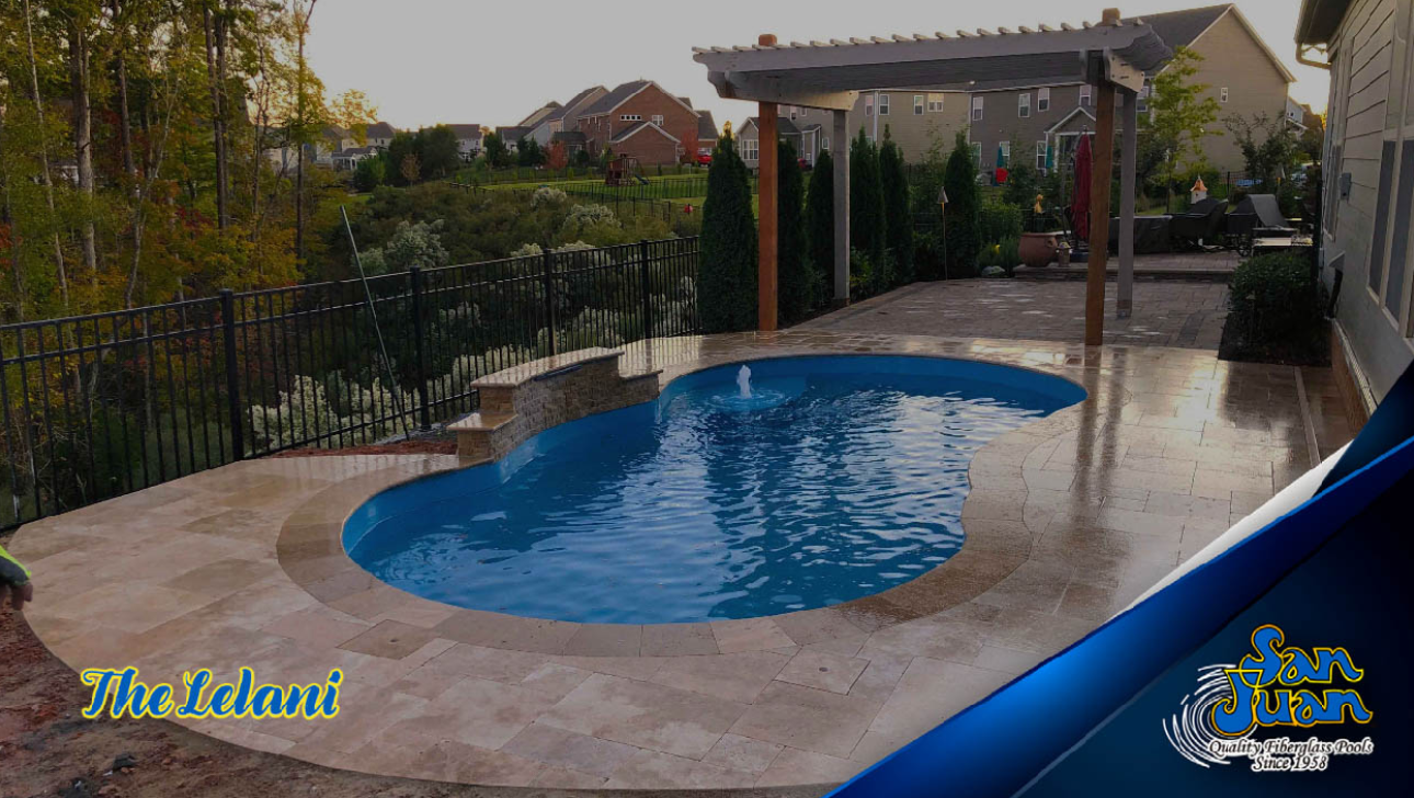 Lelani model fiberglass pool with blue water, surrounded by stone patio and fencing, featuring a pergola and landscaped backyard.